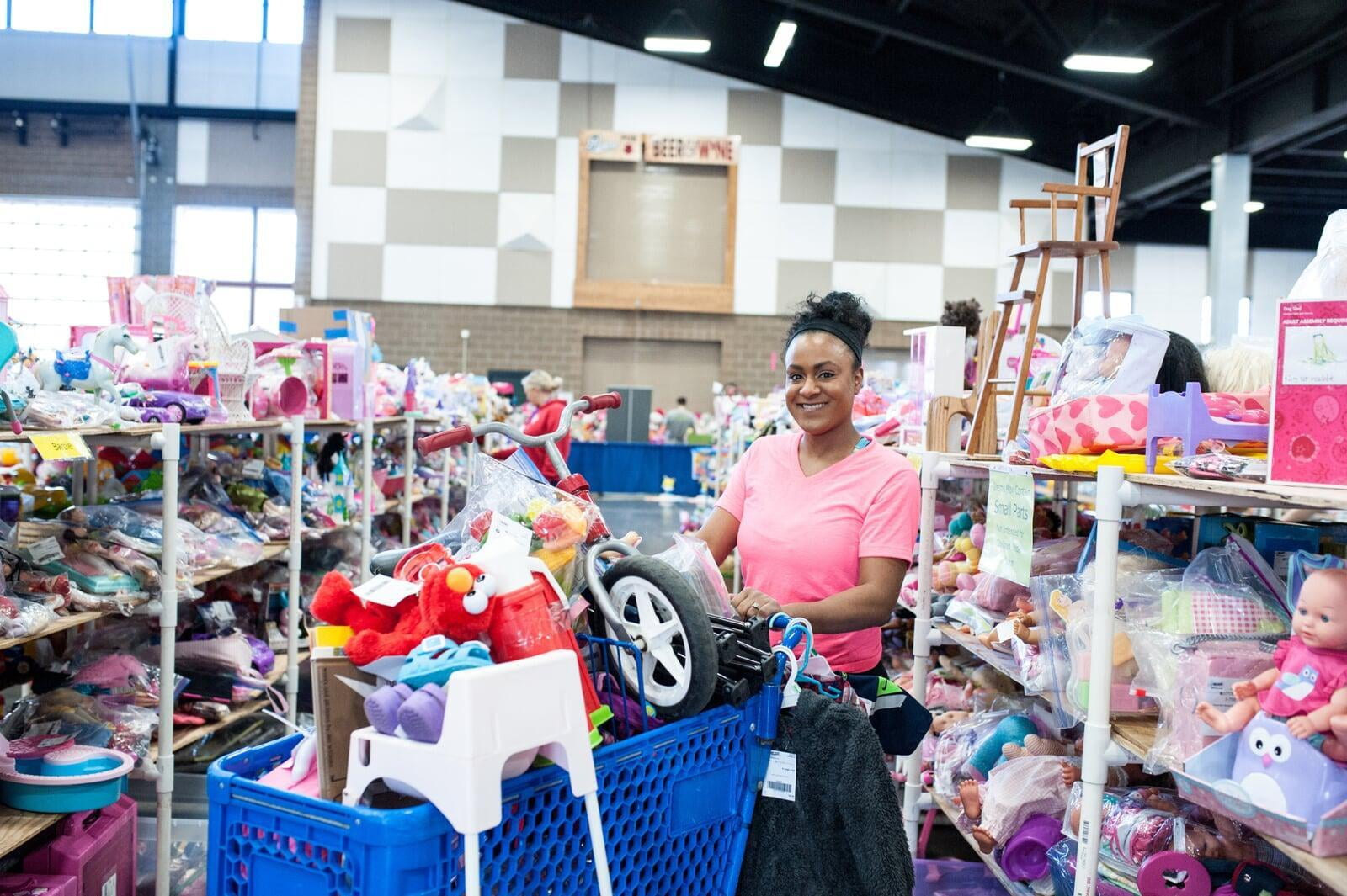 A woman shops with a shopping cart full of clothing and toys from the JBF sale.