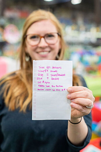 A woman smiles and holds up a shopping list